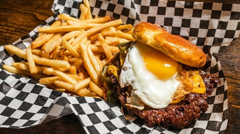 A juicy burger with a fried egg and peppers, served with a side of golden fries.